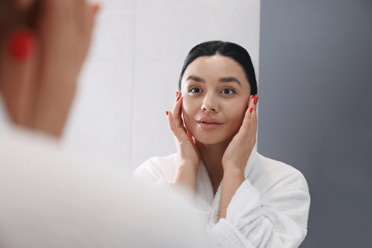 Woman looks at the mirror and touches her face.